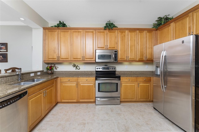 kitchen with ornamental molding, dark stone counters, stainless steel appliances, sink, and light tile patterned floors