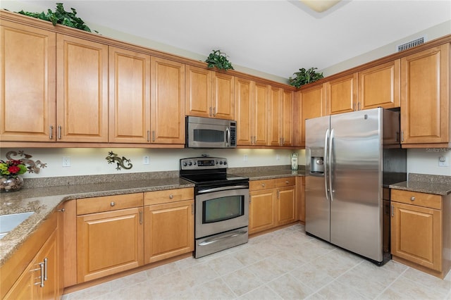 kitchen with light tile patterned flooring, stainless steel appliances, and dark stone countertops