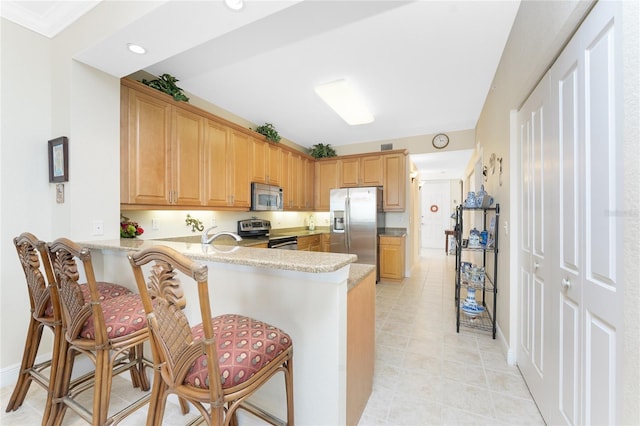 kitchen featuring a kitchen breakfast bar, light stone counters, kitchen peninsula, and appliances with stainless steel finishes