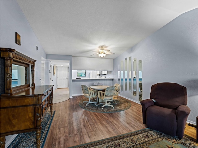 dining area with ceiling fan, wood-type flooring, a textured ceiling, and vaulted ceiling