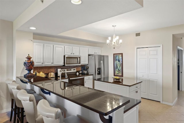 kitchen with hanging light fixtures, stainless steel appliances, white cabinetry, and tasteful backsplash