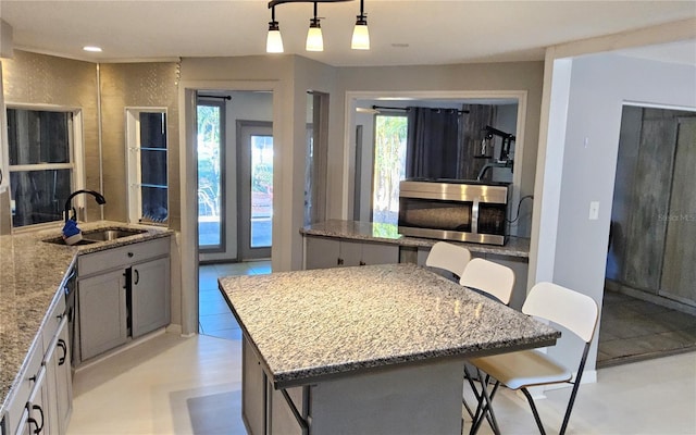 kitchen featuring a wealth of natural light, sink, light stone counters, an island with sink, and decorative light fixtures