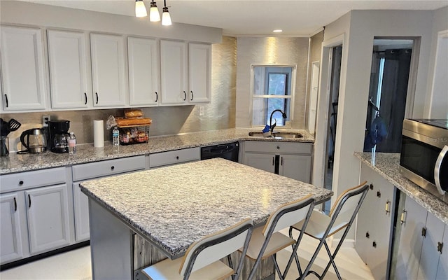 kitchen featuring light stone counters, a breakfast bar, sink, black dishwasher, and a kitchen island