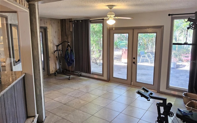 entryway with wood walls, french doors, ceiling fan, light tile patterned floors, and a textured ceiling