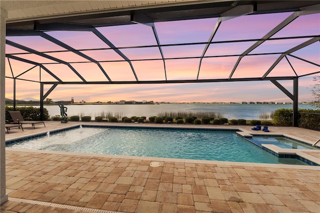 pool at dusk featuring an in ground hot tub, a water view, glass enclosure, and a patio area