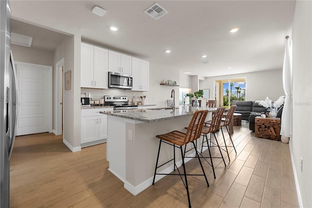 kitchen with light stone counters, a breakfast bar, white cabinets, a center island with sink, and appliances with stainless steel finishes