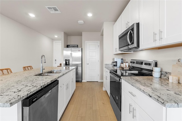 kitchen featuring white cabinetry, sink, an island with sink, light hardwood / wood-style floors, and appliances with stainless steel finishes