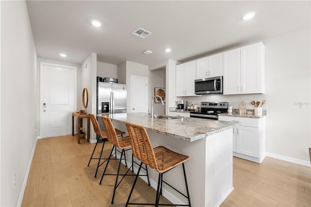 kitchen featuring a kitchen bar, light stone countertops, stainless steel appliances, white cabinets, and an island with sink