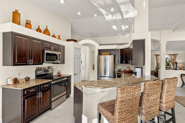 kitchen featuring light tile patterned flooring, a kitchen bar, kitchen peninsula, and stainless steel appliances