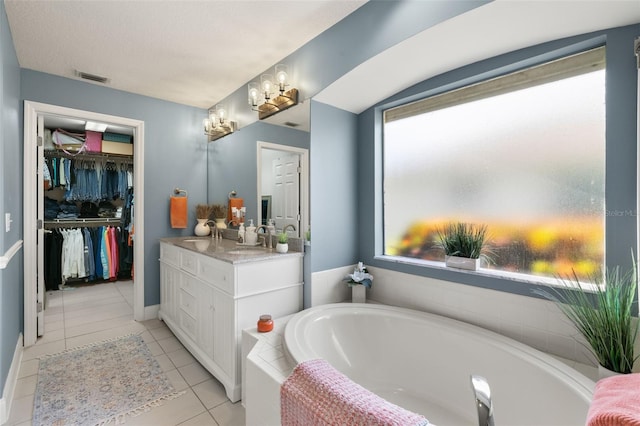 bathroom with tile patterned floors, tiled tub, plenty of natural light, and vanity