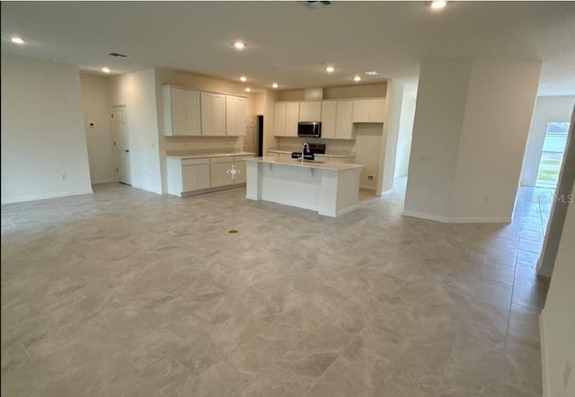 kitchen featuring stainless steel appliances, light countertops, open floor plan, white cabinets, and an island with sink