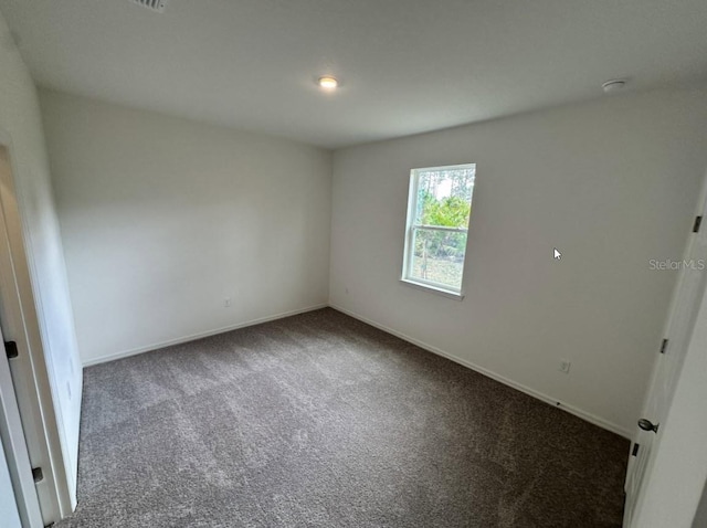 unfurnished room featuring baseboards and dark colored carpet