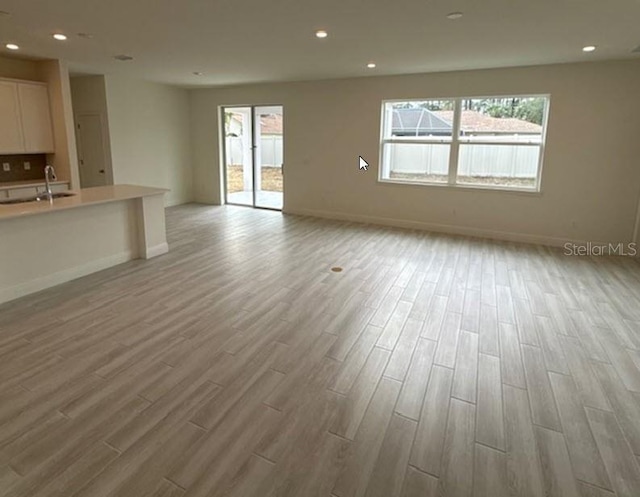 unfurnished living room featuring sink and light hardwood / wood-style floors