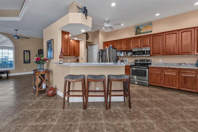 kitchen with a kitchen bar, ceiling fan, stainless steel appliances, and light stone counters