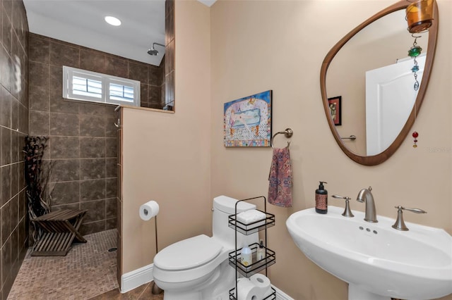 bathroom featuring toilet, a tile shower, and sink