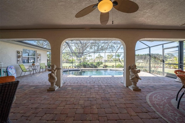 view of swimming pool featuring glass enclosure, ceiling fan, and a patio area