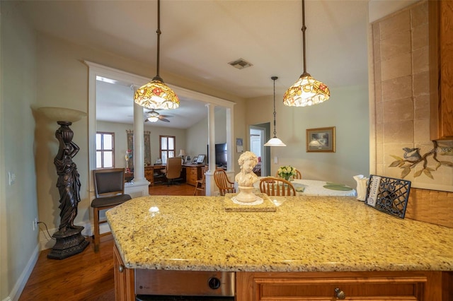 kitchen with ceiling fan, hanging light fixtures, light stone counters, dark hardwood / wood-style flooring, and decorative columns