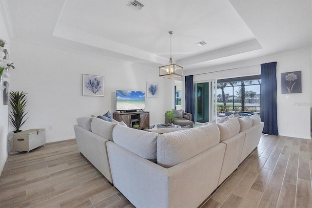 living room featuring a tray ceiling, light hardwood / wood-style flooring, and an inviting chandelier