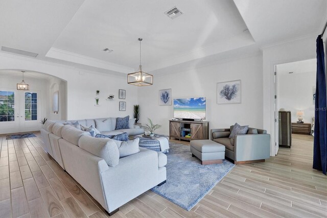 living room featuring a raised ceiling, french doors, a chandelier, and ornamental molding