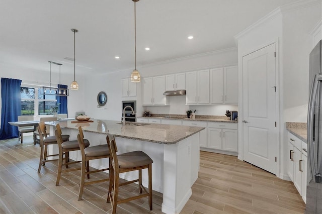 kitchen with pendant lighting, sink, a large island, a kitchen bar, and white cabinetry