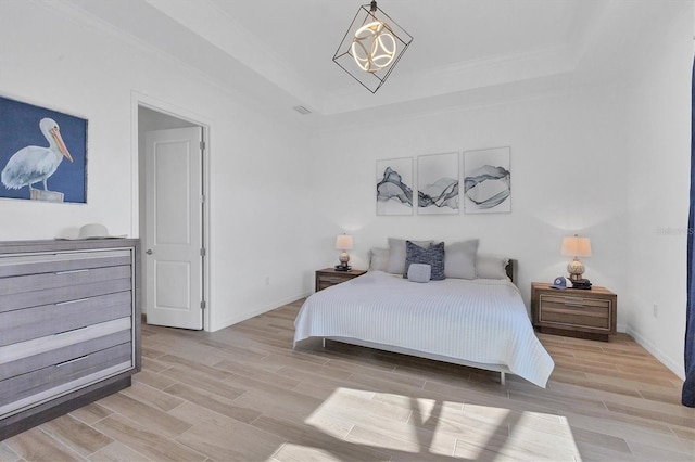 bedroom featuring a notable chandelier, light hardwood / wood-style floors, ornamental molding, and a tray ceiling