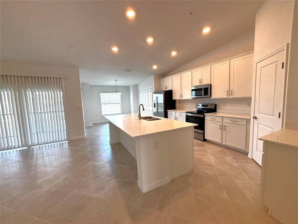 kitchen with sink, appliances with stainless steel finishes, white cabinetry, a center island with sink, and vaulted ceiling