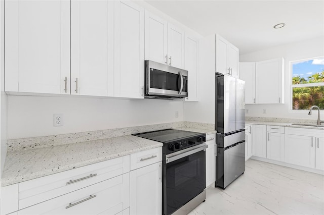 kitchen featuring appliances with stainless steel finishes, light stone counters, white cabinetry, and sink