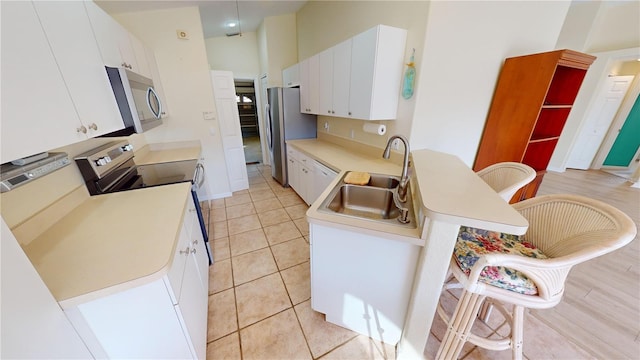 kitchen featuring appliances with stainless steel finishes, sink, white cabinetry, a breakfast bar area, and light tile patterned flooring