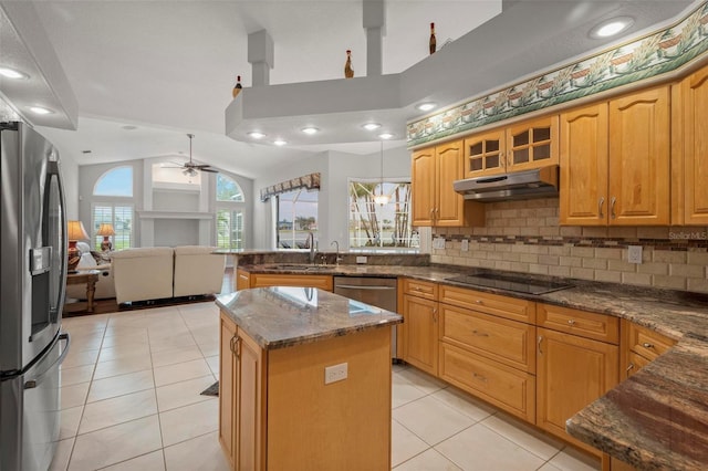 kitchen with appliances with stainless steel finishes, vaulted ceiling, ceiling fan, dark stone countertops, and a center island