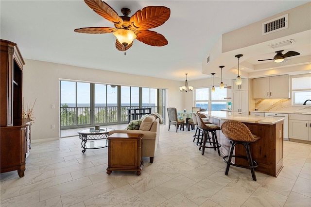 living room with ceiling fan with notable chandelier, sink, a raised ceiling, and a water view