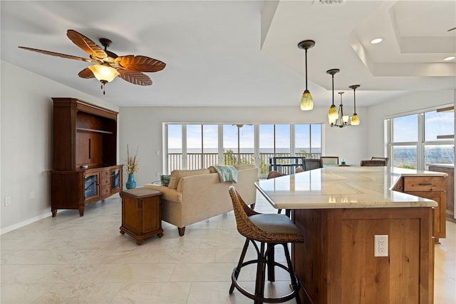 kitchen with a tray ceiling, a kitchen island, ceiling fan with notable chandelier, and pendant lighting