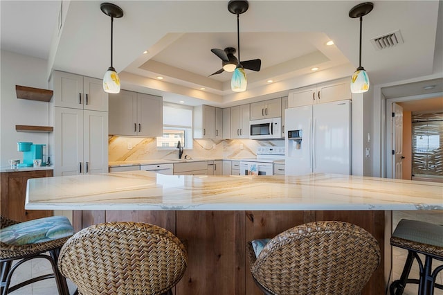 kitchen with sink, light stone counters, a tray ceiling, and white appliances