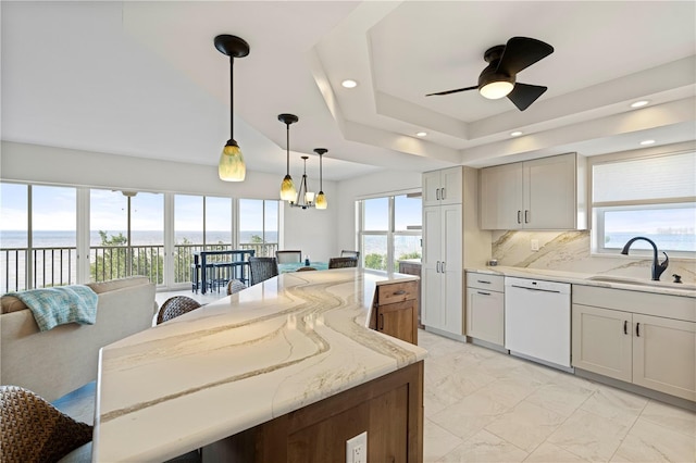 kitchen with ceiling fan, sink, white dishwasher, hanging light fixtures, and light stone countertops