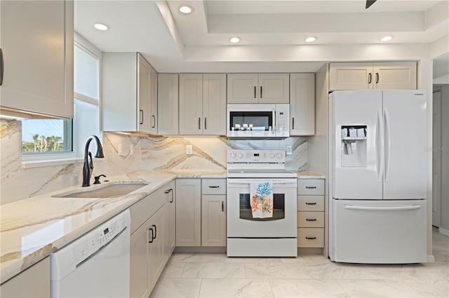 kitchen featuring white appliances, tasteful backsplash, sink, a raised ceiling, and light stone counters