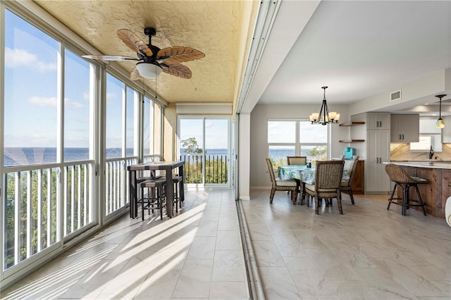 sunroom / solarium with ceiling fan with notable chandelier, a water view, and sink