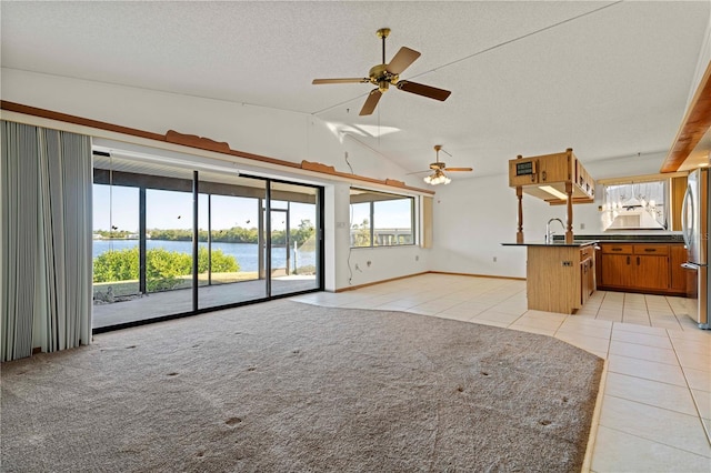 unfurnished living room featuring vaulted ceiling, ceiling fan, sink, light tile patterned floors, and a water view