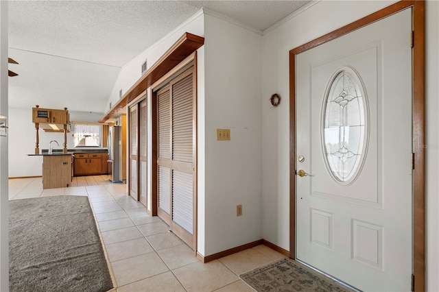 foyer entrance featuring sink, crown molding, a textured ceiling, vaulted ceiling, and light tile patterned floors