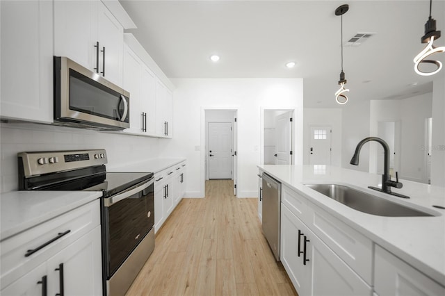 kitchen featuring appliances with stainless steel finishes, sink, white cabinets, light hardwood / wood-style floors, and hanging light fixtures