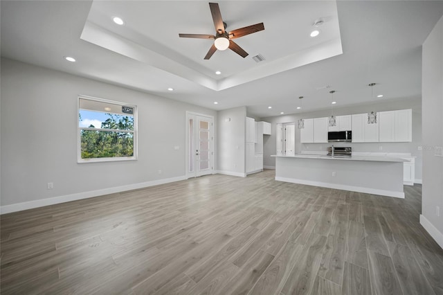 unfurnished living room featuring ceiling fan, a raised ceiling, light wood-type flooring, and sink