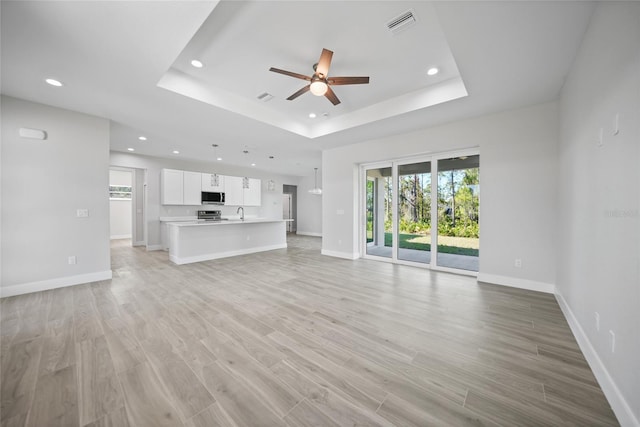 unfurnished living room featuring ceiling fan, light wood-type flooring, and a tray ceiling