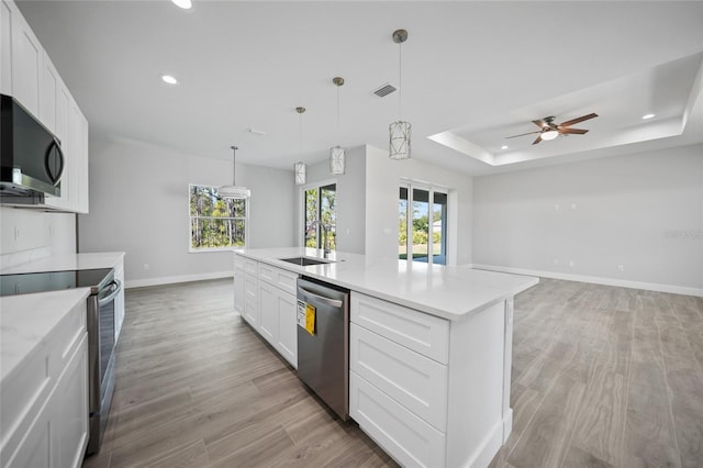 kitchen featuring sink, a raised ceiling, a kitchen island with sink, white cabinets, and appliances with stainless steel finishes