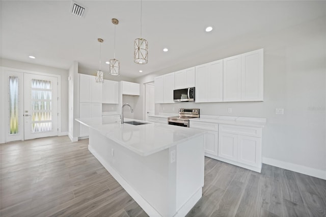 kitchen with appliances with stainless steel finishes, sink, decorative light fixtures, white cabinets, and an island with sink