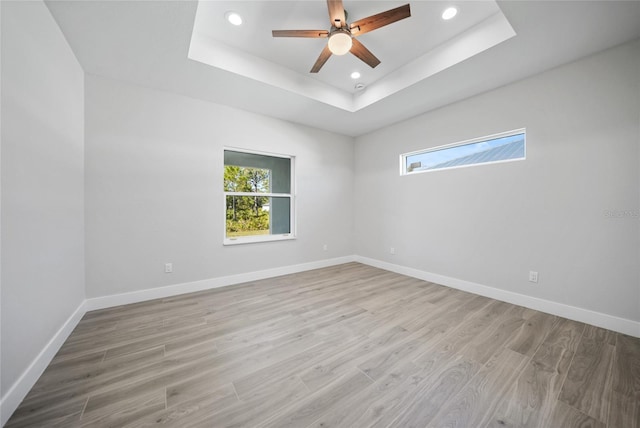 spare room with a raised ceiling, ceiling fan, and light hardwood / wood-style floors