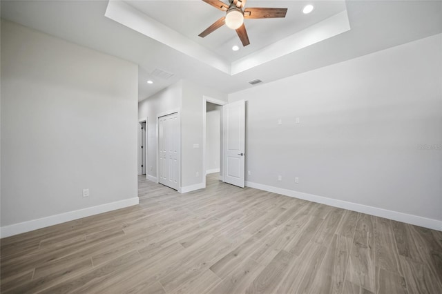 empty room with ceiling fan, light hardwood / wood-style flooring, and a tray ceiling