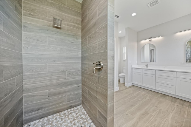 bathroom with tiled shower, vanity, hardwood / wood-style flooring, and toilet