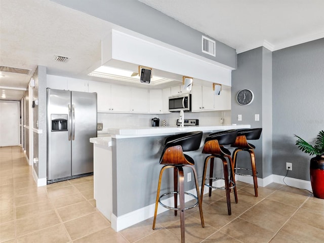 kitchen featuring a kitchen breakfast bar, kitchen peninsula, white cabinetry, and appliances with stainless steel finishes