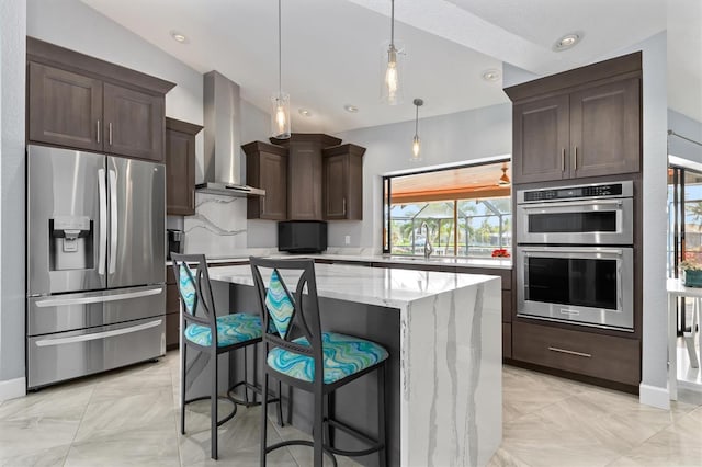 kitchen with light stone countertops, stainless steel appliances, wall chimney range hood, pendant lighting, and a kitchen island