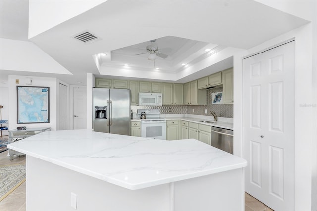 kitchen featuring stainless steel appliances, tasteful backsplash, ceiling fan, light stone counters, and a tray ceiling