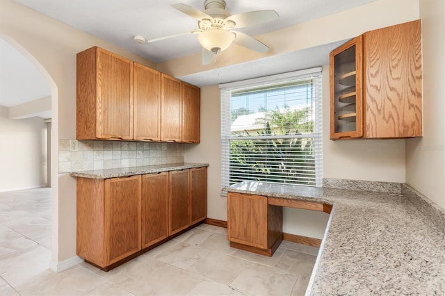 kitchen featuring ceiling fan, light stone counters, and backsplash