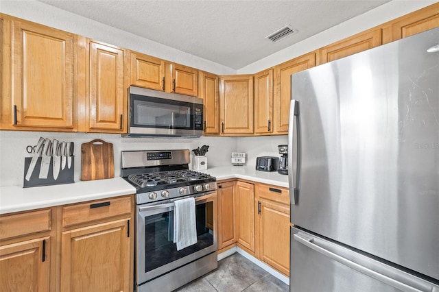 kitchen featuring stainless steel appliances, light tile patterned flooring, and a textured ceiling